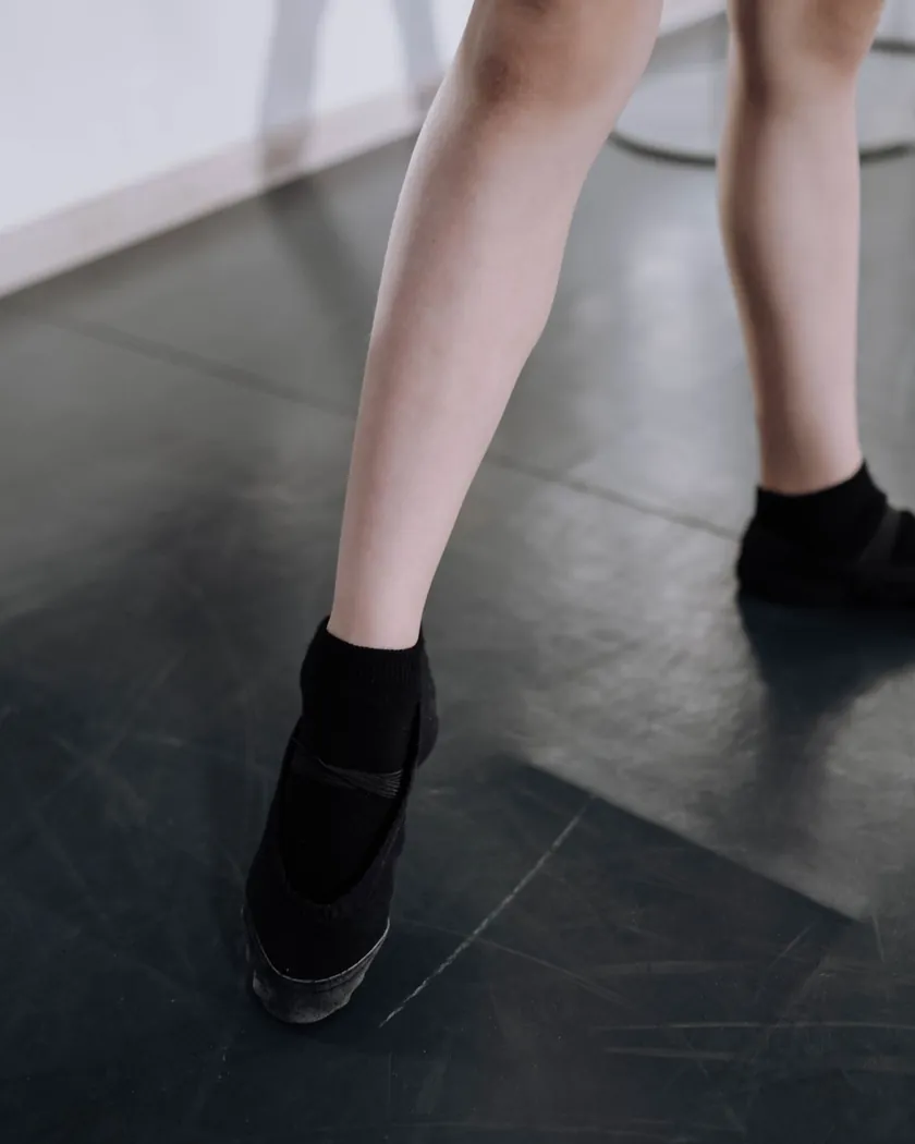 Pies y tobillos de una bailarina apoyados sobre el suelo oscuro de una sala de ensayo