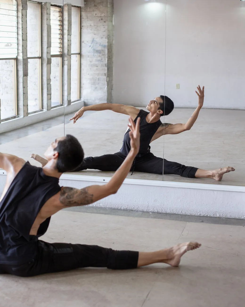 Bailarín estirando en el suelo de una sala de ensayo junto a una pared de espejos